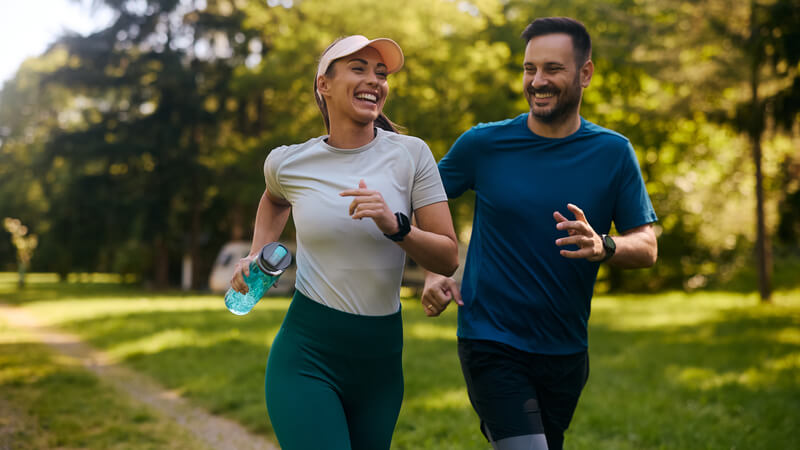 Young smiling couple running side by side through park.