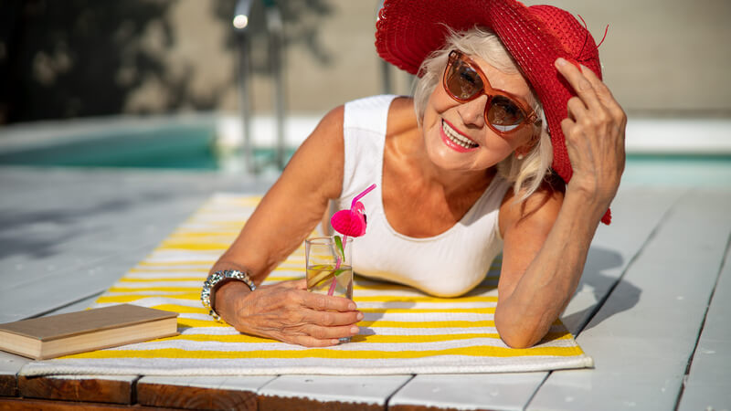 Smiling older woman in a red sun hat beside a pool.