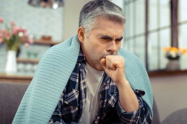 Man sitting, coughing, with blanket over his shoulders