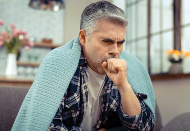 Man sitting, coughing, with blanket over his shoulders